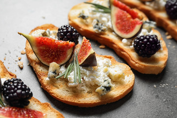 Bruschettas with cheese, figs and blackberries on grey table, closeup