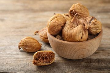 Bowl and tasty dried figs on wooden table. Space for text