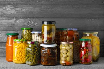 Jars with pickled vegetables on wooden table against grey background