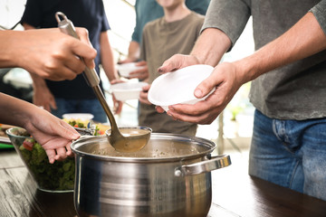 Volunteer serving food to poor people in charity centre, closeup