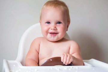 A young child sits in a highchair and eats cottage cheese. Finger food for the development of fine motor skills. Smiling little girl.