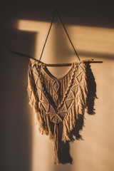 Macrame wall hanging in the sunny spot of the room. DIY boho wall tapestry hanging on the wall in...