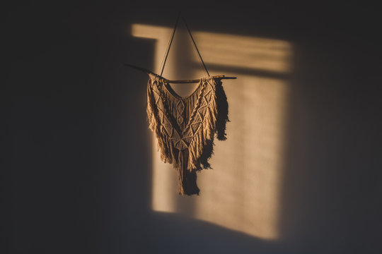 Macrame wall hanging in the sunny spot of the room. DIY boho wall tapestry hanging on the wall in the morning sun