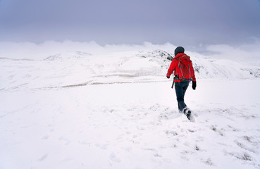 Fototapeta na wymiar A hiker walking through fresh snow while descending from the summit of High Raise towards Rampsgill Head near Hartsop in the Lake District.