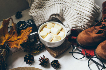 Cozy autumn morning with cup of coffee with cream and autumn leaves, autumn clothes and glasses Autumn and holiday concept