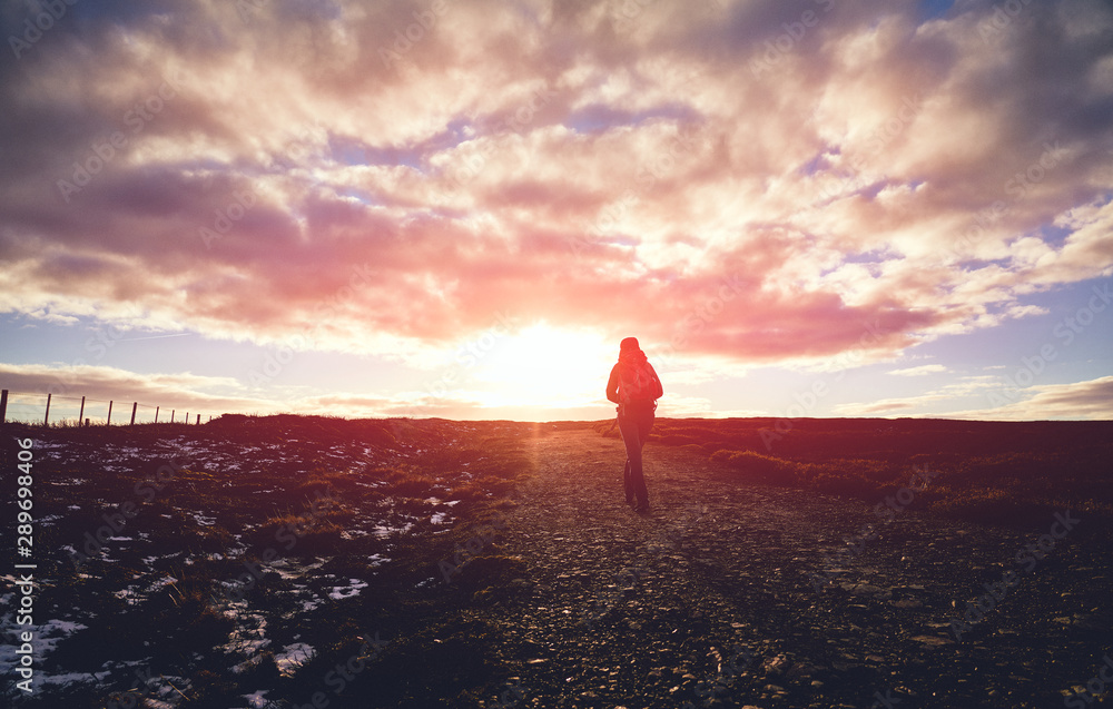 Wall mural The silhouette of a hiker walking into the sunset across a moorland trail.