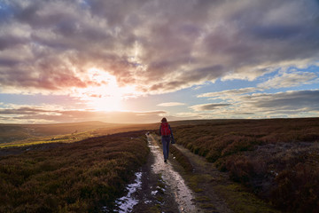 A hiker centre frame walking straight towards a sunset on open heather moors at Edmundbyers.