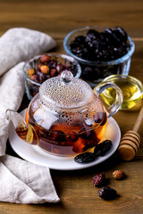 Glass Teapot of Hot Tea with Dried Rose Heap or Dog Rose Bowl with Dried Dog Rose and Glass Bowl with Dried Plums Autumn Healthy Diet Drink and Food Vertical Honey