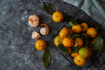 Naklejka na ściany i meble Juicy tangerines with leaves in a basket on a dark background