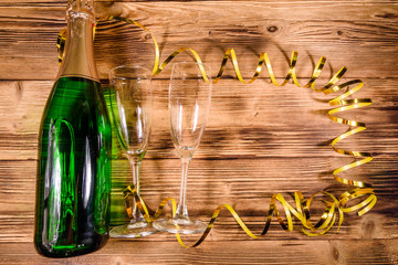 Bottle of champagne and two wineglasses decorated with golden ribbon on wooden table. Top view