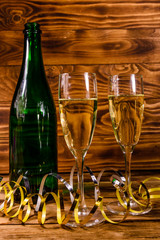 Bottle of champagne and two wineglasses decorated with golden ribbon on wooden table