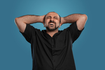 Close-up portrait of a brunet middle-aged man with beard, dressed in a black t-shirt and posing against a blue background.