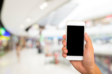 Fototapeta na wymiar Hand hold black smartphone on blur shopping mall background