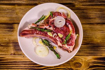 Raw ribeye steak, spices, rosemary, onion and garlic in a ceramic plate on wooden table. Top view