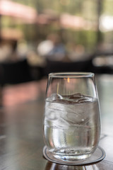 A glass of water with ice place on a dark brown wooden table with a paper coaster under a glass