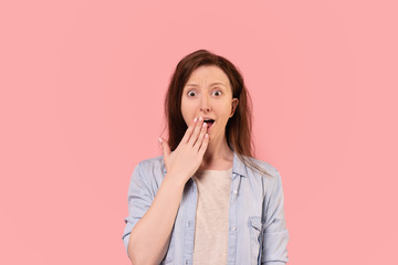 Portrait of a shocked joyful young red-haired woman in casual clothes posing on a pink background. Emotional caucasian woman happy about unexpected discounts. Advertising space
