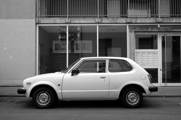 Weißer japanischer Kleinwagen der Siebzigerjahre mit drei Türen vor verglastem Hauseingang im...