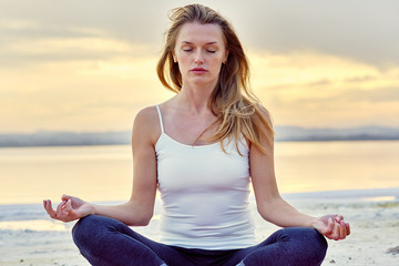 Fototapeta na wymiar Alone yogi woman seated in lotus position meditating near lake