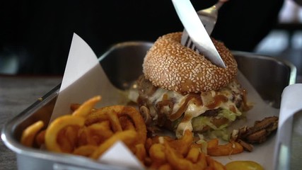 Cutting swiss cheese beef burger mushroom and curly fries in tray