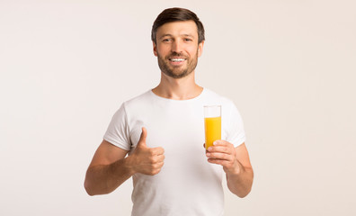 Fototapeta premium Man Holding Glass Of Juice Gesturing Thumbs-Up In Studio