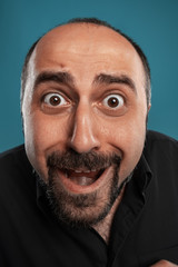 Close-up portrait of a brunet middle-aged man with beard, dressed in a black t-shirt and posing against a blue background.
