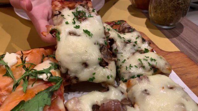 Hands gets pizza slice from breadboard at restaurant table, food concept, slow motion close up