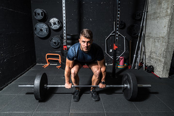 Naklejka na ściany i meble Young strong fit muscular sweaty man with big muscles doing heavy barbell weight lifting workout cross training in the gym real people