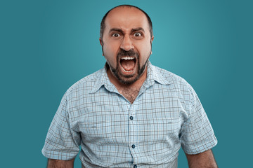 Fototapeta premium Close-up portrait of a brunet middle-aged man with beard, dressed in a light checkered shirt and posing against a blue background.
