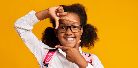 Smiling Black School Girl Looking Through Fingers Frame, Yellow Background