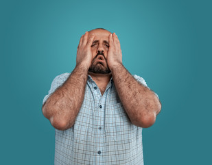 Close-up portrait of a brunet middle-aged man with beard, dressed in a light checkered shirt and posing against a blue background.