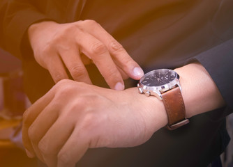 Close-up of watch on wrist of man. Men in black shirt looking at his luxury watches brown leather...