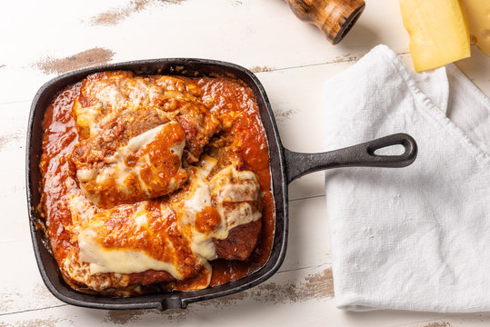 Parmegiana Steak also known as Filet Parmegiana in a black iron pan on a wooden white background, cheese and tomato sauce. Soft light, top view. Flat layer
