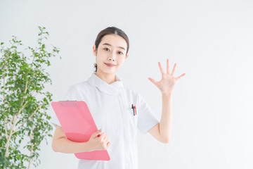 指で「5」をつくる白衣の女性