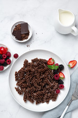 Chocolate fusilli pasta with fresh berry on white plate