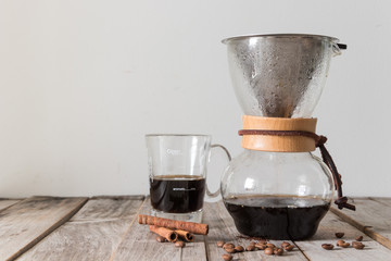 Homemade drip coffee using glass jug and metal filter with beans on wooden table over white background