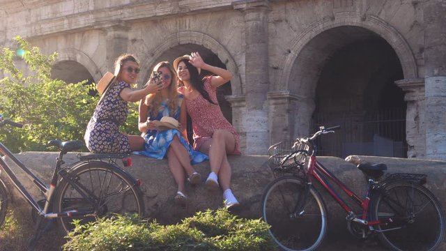 Three happy young women friends tourists with bikes taking selfies at Colosseum in Rome, Italy at sunrise.