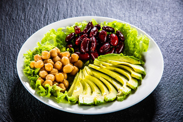 Vegetable salad with chickpea, avocado and red beans in bowl on black stone 