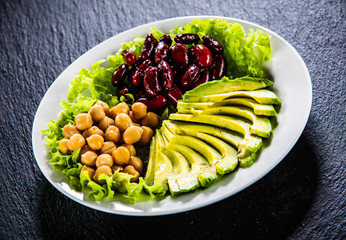 Vegetable salad with chickpea, avocado and red beans in bowl on black stone 