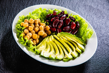 Vegetable salad with chickpea, avocado and red beans in bowl on black stone 
