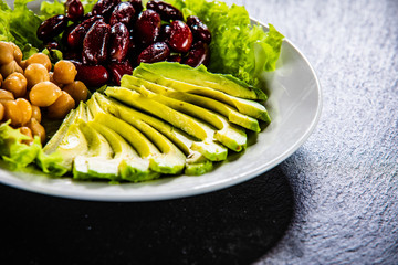 Vegetable salad with chickpea, avocado and red beans in bowl on black stone 