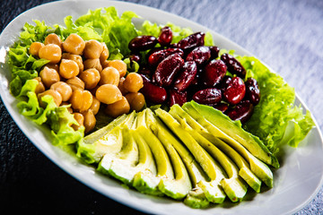 Vegetable salad with chickpea, avocado and red beans in bowl on black stone 