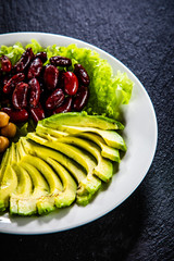 Vegetable salad with chickpea, avocado and red beans in bowl on black stone 