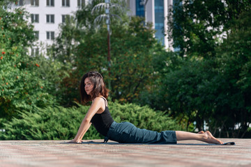 young girl in the park is doing yoga asana near a building of a business center