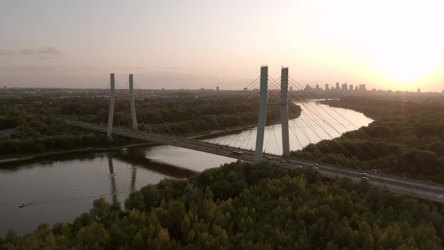 Aerial view of the Warsaw city skyline, Siekierkowski Bridge and city skyline skyscrapers in the background, yellow sunset. Cars passing over the bridge. Drone Shot 4K.
