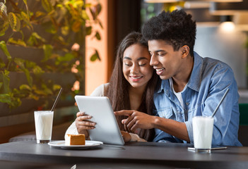 Teen couple in cafe using digital tablet and laughing