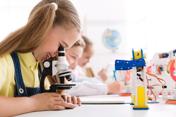 Girl looking at microscope with robot nearby