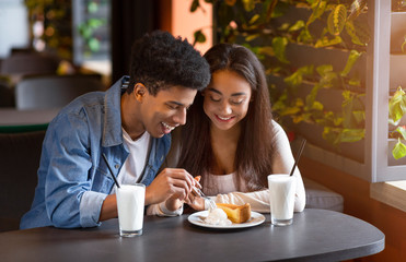 Couple of teenagers eating cheesecake with ice cream at cafe