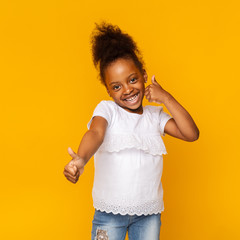 Cute shy little afro girl gesturing thumbs up and smiling - obrazy, fototapety, plakaty
