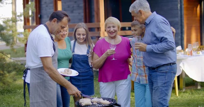Grandchildren join senior grandparents preparing barbecue, family enjoying summertime outdoors. 4K UHD