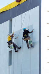 Fototapeta premium pintores colgados de un arnés pintando una fachada